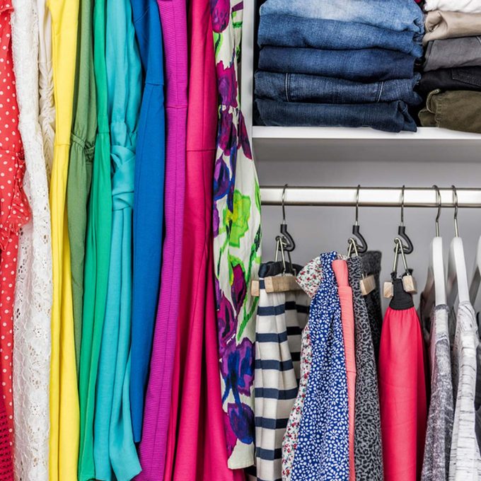 Colorful dresses and tops hang alongside neatly folded jeans in a closet, showcasing a variety of fabrics and styles in an organized arrangement.