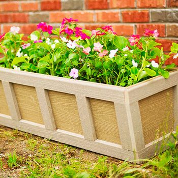 Colorful flowers bloom in a wooden planter, showcasing shades of pink and green, set against a textured red brick wall.