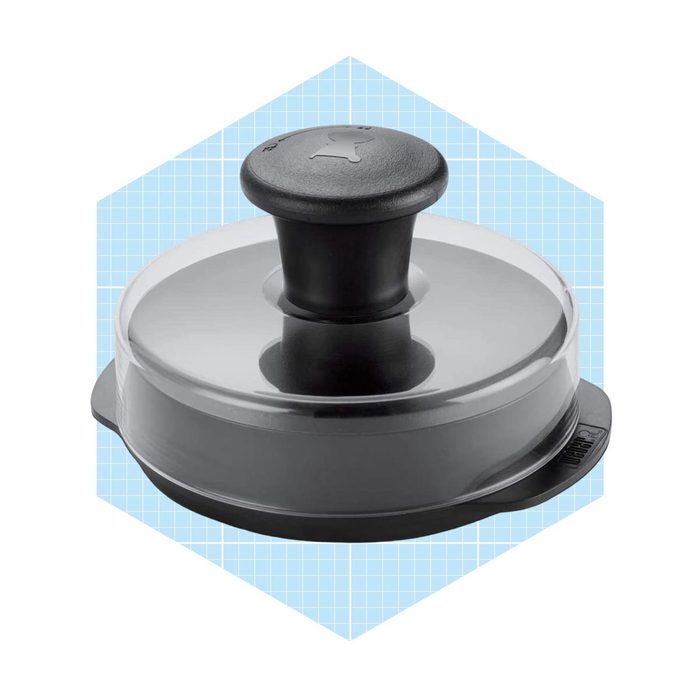 A black and clear burger press is positioned upright, designed for shaping patties, resting on a light blue grid-patterned background.