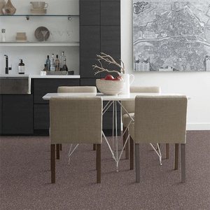 A dining table surrounded by four chairs holds a bowl of apples, set against a modern kitchen backdrop with dark cabinetry and a wall map.