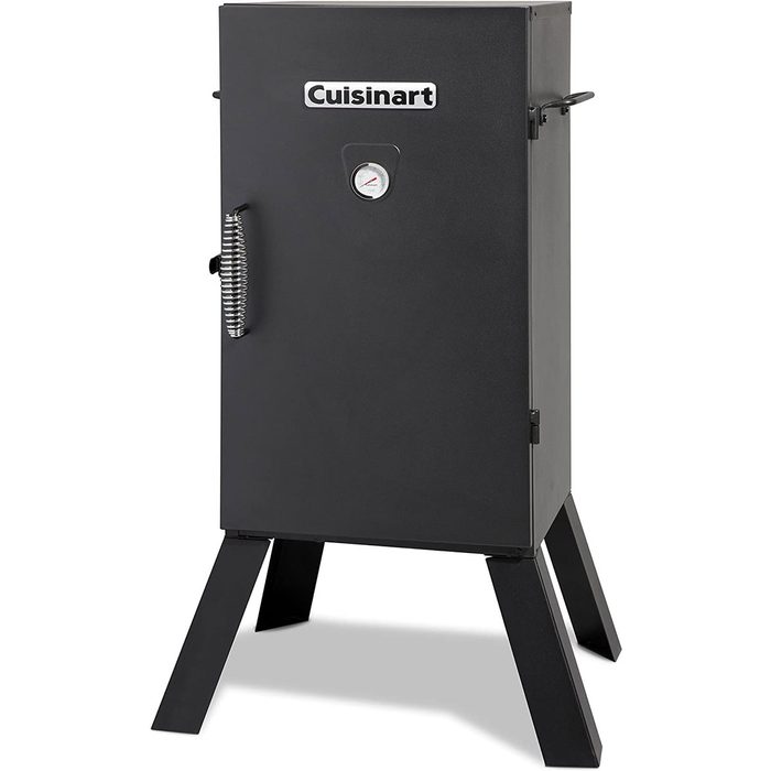 A black vertical smoker stands on four legs, featuring a circular temperature gauge and a handle, designed for outdoor cooking.