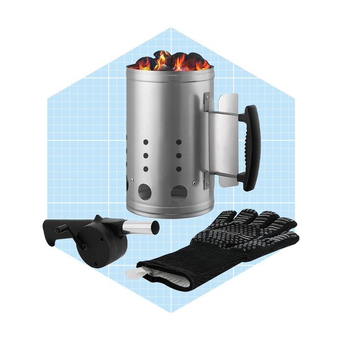 A metallic charcoal chimney filled with glowing coals emits flames, accompanied by a grilling tool and safety gloves against a light blue grid background.