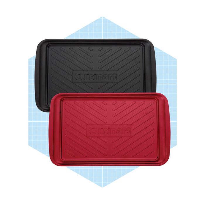 Two baking trays, one black and one red, are stacked slightly askew on a light blue grid background, featuring textured surfaces and visible brand name.