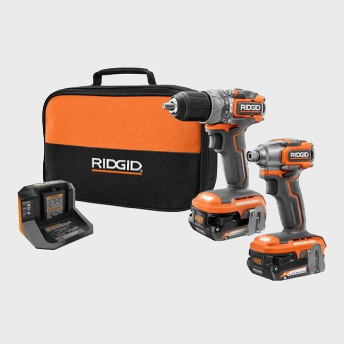 Two cordless power tools, a drill and an impact driver, are positioned next to a battery charger and a black and orange carrying case.