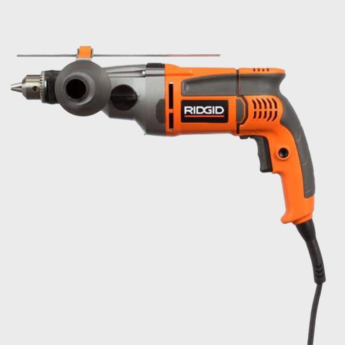 A power drill rests horizontally, with a gray and orange exterior. It features a chuck at the front and a power cord extending from the handle.