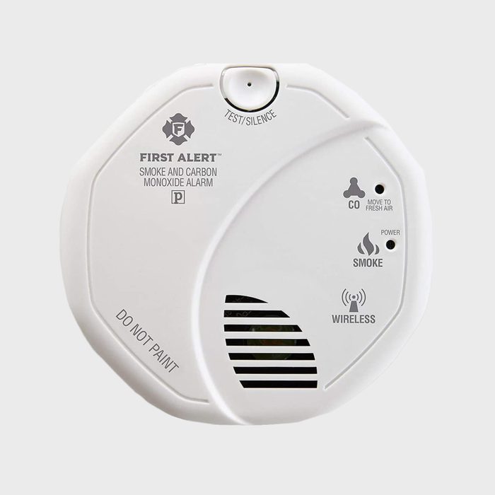 A white smoke and carbon monoxide alarm hangs on a wall, indicating test/silence options, with warnings about carbon monoxide, smoke detection, and being wireless.