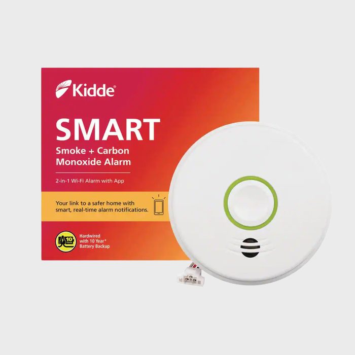 A white smoke and carbon monoxide alarm is displayed beside its packaging, featuring bright colors and text promoting smart, real-time notifications for safety.