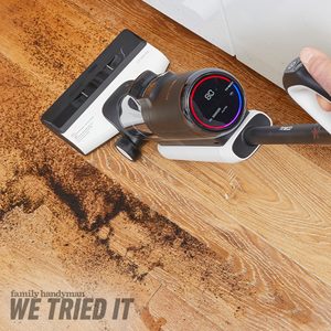 A vacuum cleaner is removing dirt from a wooden floor, while a digital display shows its operational status. Dark debris is visible on the floor.