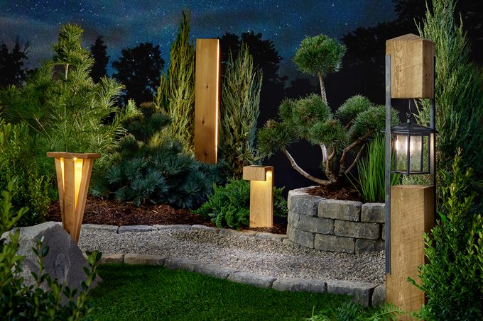 Stylish outdoor lights illuminate a landscaped garden at night, surrounded by various greenery and stone features, creating a serene ambiance.