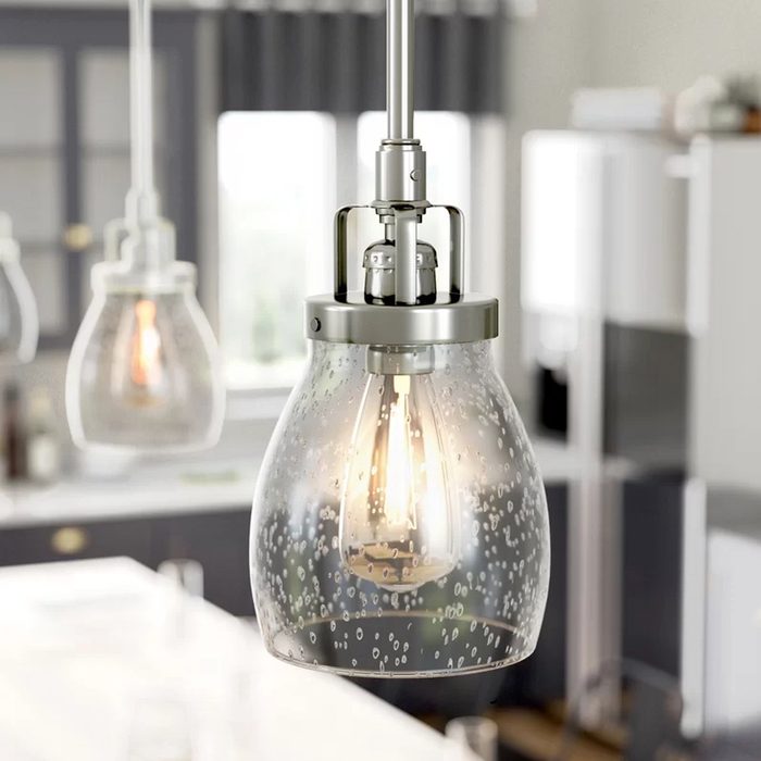 A glass pendant light illuminates a modern kitchen, showcasing bubbles within its shade. The background features cabinetry and a bright, airy atmosphere.