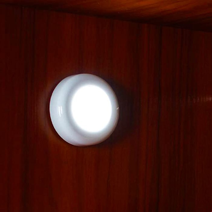 A round, white lamp emits light, mounted on a dark wooden wall surface, illuminating its surroundings softly.