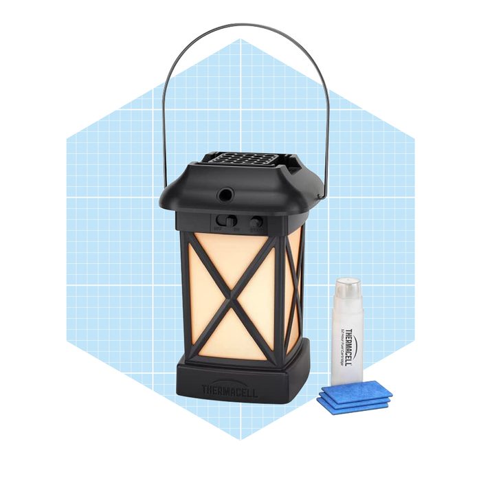 A black and cream lantern emits light while a bottle and blue pads sit nearby, suggesting use for outdoor activities in a clean, geometric background.