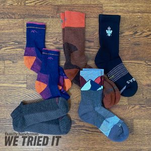 A variety of colorful socks are arranged on a wooden surface, showcasing different patterns and textures, with a magazine title partially visible below.