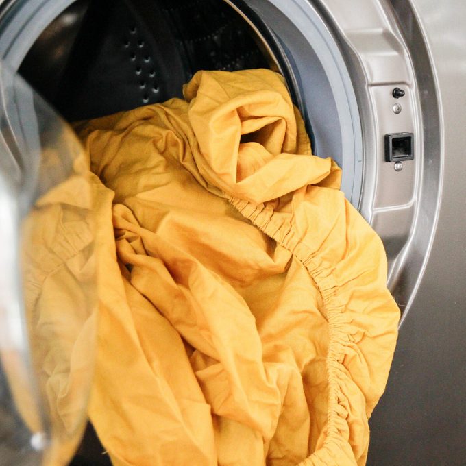 Yellow fitted sheet spilling out of a washing machine